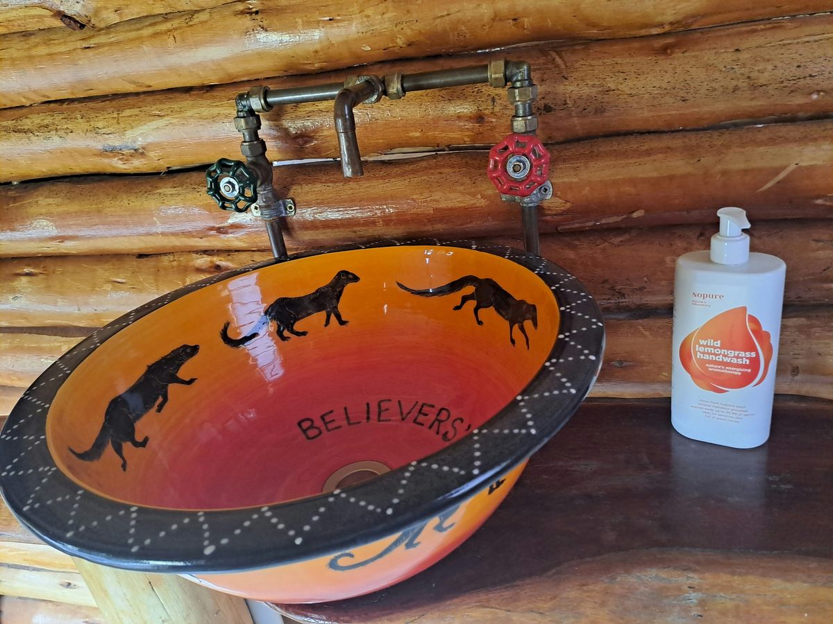 A hand-painted basin with black meerkat silhouettes on orange, set into a log wall