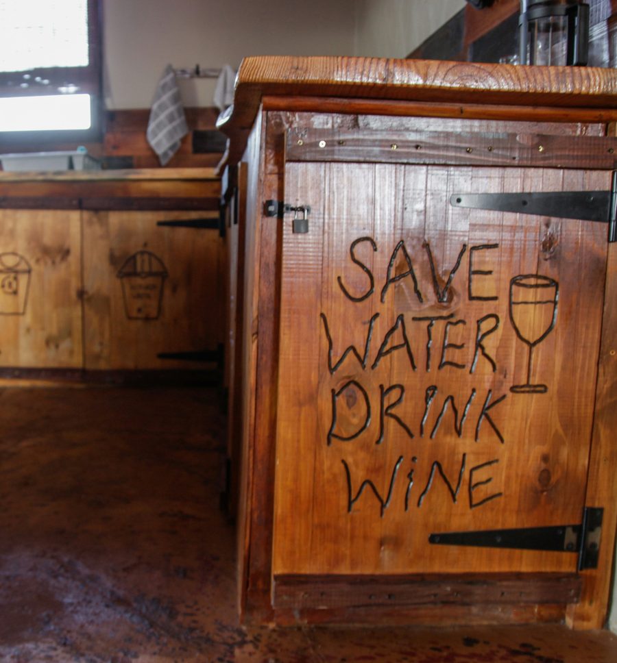 A wooden kitchen cupboard door with "Save water, drink wine" burned into it