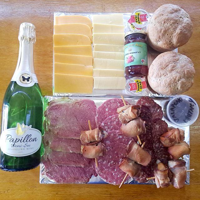 A celebration platter with bubbly, cheeses, cold meats and fresh bread rolls